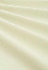 Tissu en coton d'une douce couleur crème, présentant de subtils reliefs texturés, tombant doucement en plis.