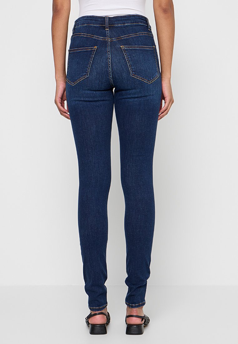 Schmale Jeans aus dunkelblauem Denim mit hoher Taille, Fünf-Taschen-Design und kontrastierenden orangen Nähten. Glatte Textur und taillierte Form.