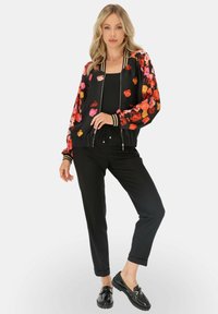 Bomberka z kwiatowym wzorem na czarnym tle, z wyrazistymi różowymi i pomarańczowymi kwiatami, ściągaczami na rękawach oraz zamek błyskawiczny, połączona z czarnymi spodniami i czarnymi butami.