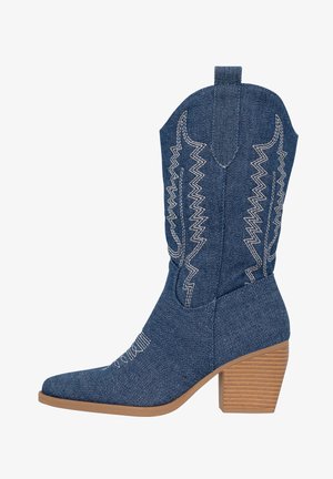 Denim cowboy boot with pointed toe and tapered shape, featuring white zigzag stitching and a stacked wooden heel.
