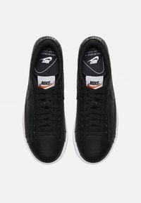 Zapatillas de cuero negro con diseño de cordones, que cuentan con una suela de goma blanca y detalles de la marca en la lengüeta y el lateral. Textura suave.