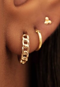 Goldene Ohrhänger mit einem massiven Kettendesign und einer glatten Oberfläche; kombiniert mit einem kleinen goldenen Steck-Ohrhänger in Form eines Schmetterlings.