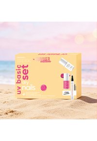 Ensemble de base UV pour ongles secs avec vernis à ongles rose, top coat et stylo soin présentés sur du sable avec la mer et le ciel en arrière-plan.