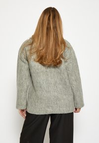 Gai pelēks filca džemperis ar taisnstūra formu, platām piedurknēm un teksturētu virsmu, apvienots ar melnām biksēm.