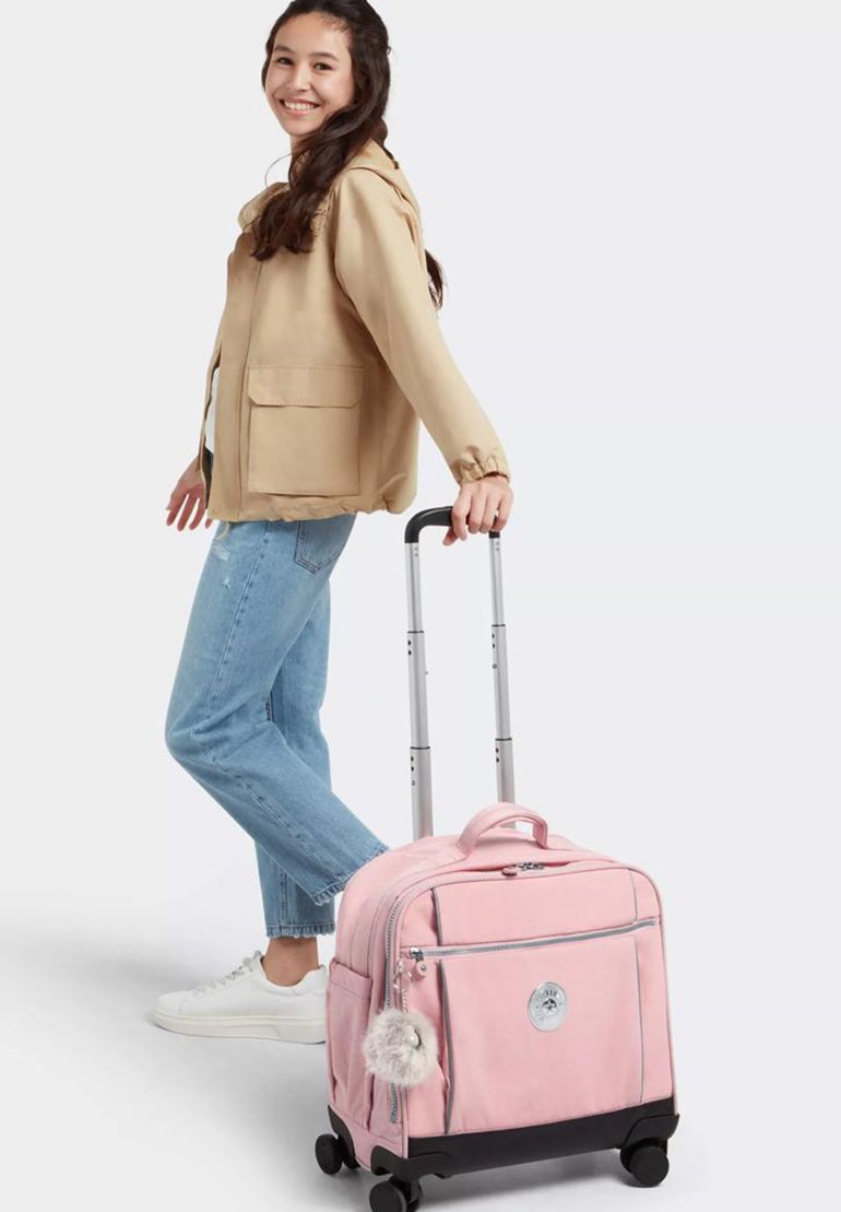 Equipaje de ruedas rosa con acentos negros, bolsillo con cremallera y un llavero de pom-pón de peluche. Tejido suave con forma rectangular y asa retráctil.