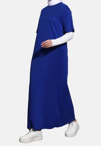 Plynulá modrá maxi šaty z měkké látky, s krátkými rukávy a kulatým výstřihem, doplněné o bílé tenisky.