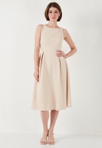 Beige bezramínková šaty s kulatým výstřihem, plisovanou sukní a volným siluetou. Hladká textura, ke kolenům s minimálními detaily.