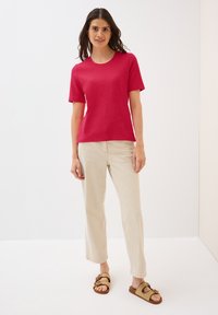 Tætsiddende kortærmet t-shirt i lys pink, kombineret med lysebeige lige bukser og brune vævede sandaler. Glat tekstur og klassisk design.