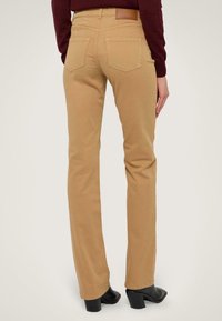 Pantalones beige de pierna recta hechos de algodón, con bolsillos traseros, que presentan una etiqueta de marca en la cintura y costuras planas. Botas de tacón negras.