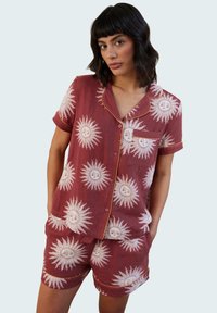 Red pajama set featuring a sun pattern, short-sleeved button-up shirt and shorts, with white designs and yellow trim accents.