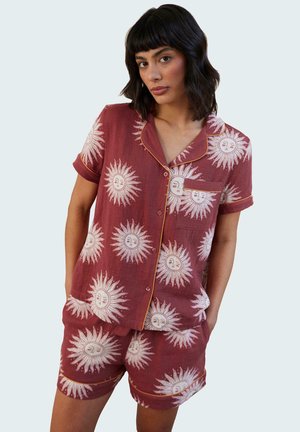 Ensemble de pyjama rouge avec un motif de soleil, chemise à manches courtes avec boutons et short, décoré de motifs blancs et de bordures jaunes.