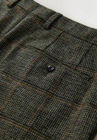 Hose aus Wolle mit Karomuster in Grün-, Braun- und Orangetönen. Mit einer Gesäßtasche mit einem dunklen Knopf und strukturiertem Stoff.