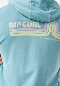Jasnoniebieska bluza z kapturem o miękkiej teksturze. Z przodu widnieje napis "RIP CURL" dużymi literami, a na plecach znajdują się kolorowe paski w odcieniach różu, żółci i niebieskiego.