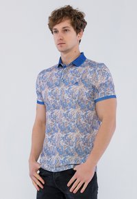 Polo de manga corta con un patrón texturizado en azul y beige, con un cuello y puños azules lisos. Botones en la parte frontal.