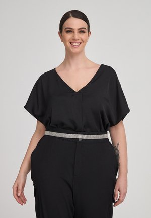 Blusa nera morbida con scollo a V e maniche corte; abbinata a pantaloni neri a vita alta e una cintura in strass argentato.