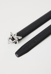 Zwart nepleer riem met een gevlochten textuur en een zilveren gespsluiting met een logoontwerp. Glad afgewerkte band.