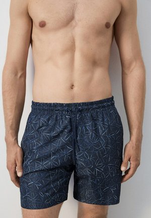 Man zonder shirt, droeg marineblauwe zwemshorts met een lichtblauw zeesterrenpatroon en een elastische tailleband met trekkoord.