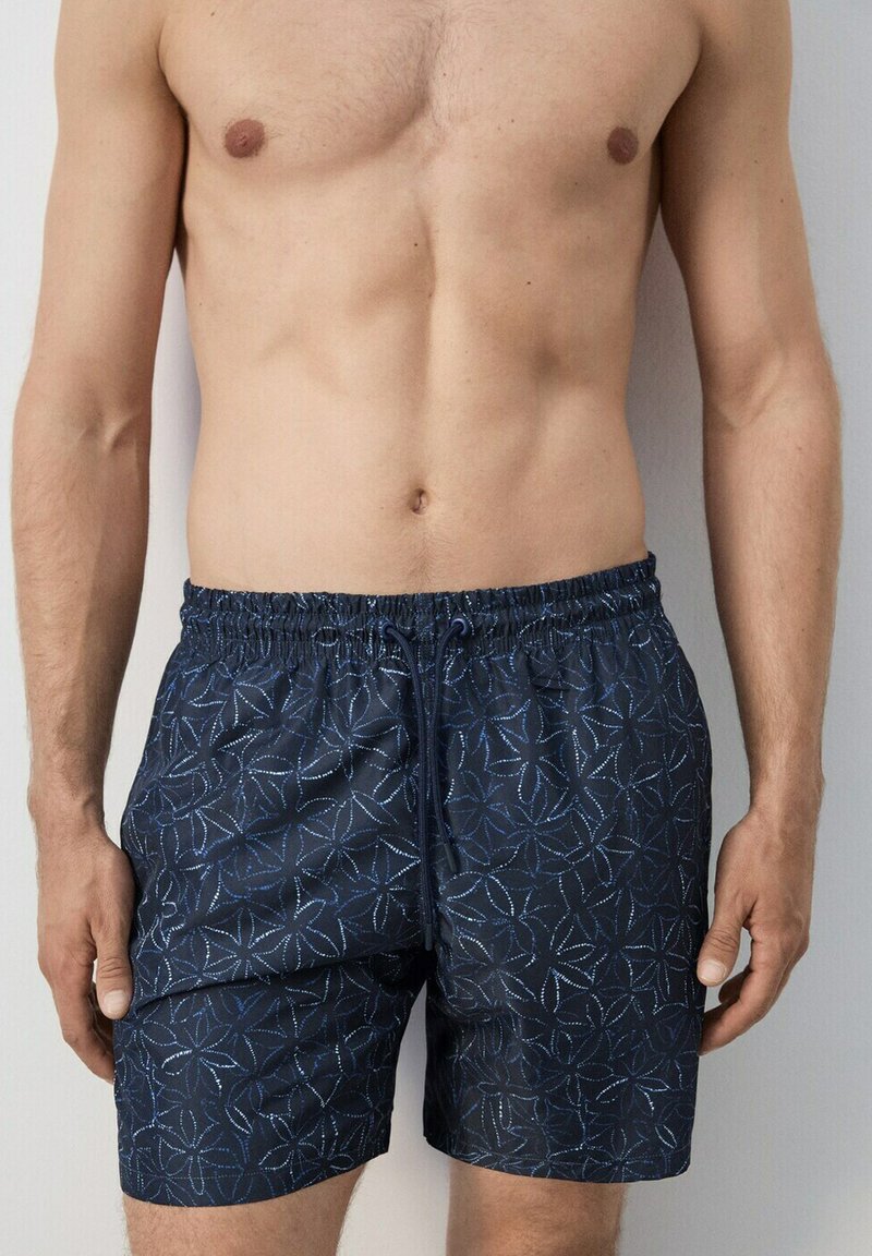 Homme torse nu portant un short de bain bleu marine avec un motif d'étoile de mer bleu clair et une taille élastique avec cordon de serrage.