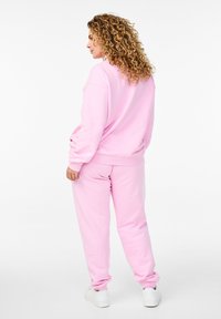 Conjunto de sudadera y pantalones de chándal de algodón rosa, con un corte relajado, puños acanalados y textura suave, combinado con zapatillas blancas.