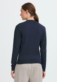 Granatowy sweter dzianinowy z długimi rękawami, okrągłym dekoltem i ściągaczem na dole. Materiał wydaje się miękki i gładki, bez widocznych wzorów czy akcentów.