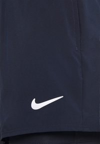 Pantaloncini sportivi blu navy con il logo Nike a forma di swoosh bianco vicino all'orlo e una tasca laterale visibile.
