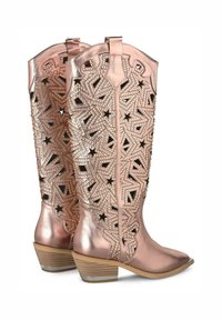 Stivali da cowboy in oro rosa con elementi geometrici ritagliati e motivi a stella, punta affusolata e tacco in legno impilato.