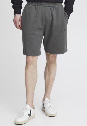 Grå bomuldsshorts med elastisk talje, sidelommer og et logo på venstre ben. Bæres med hvide sneakers.