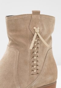 Beżowe zamszowe botki za kostkę o teksturowanym wykończeniu, z bocznym detalem w postaci sznurowania i brązowym, warstwowym obcasem. Szew na krawędziach.