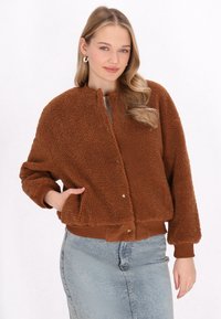 Hnědá, nadýchaná fleecová bomber bunda s kulatým límcem, patentkami a žebrovanými manžetami; ve spojení se světle modrou denimovou sukní.