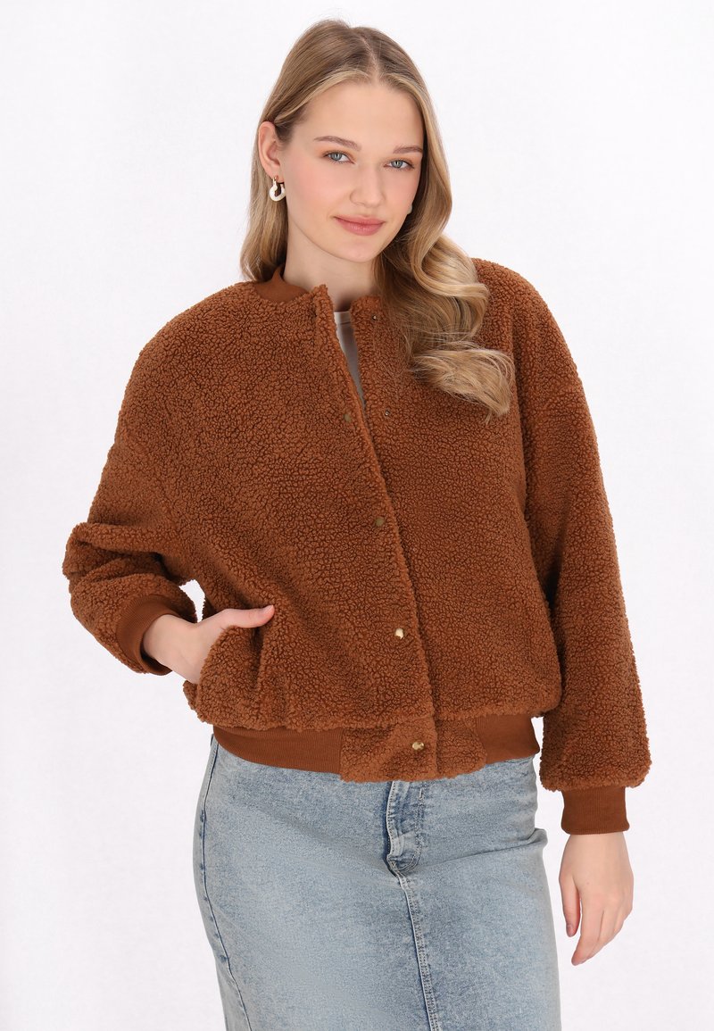 Brun, fluffig fleece-bomberjacka med rund krage, tryckknappar och ribbade manschetter; kombinerad med en ljusblå jeanskjol.
