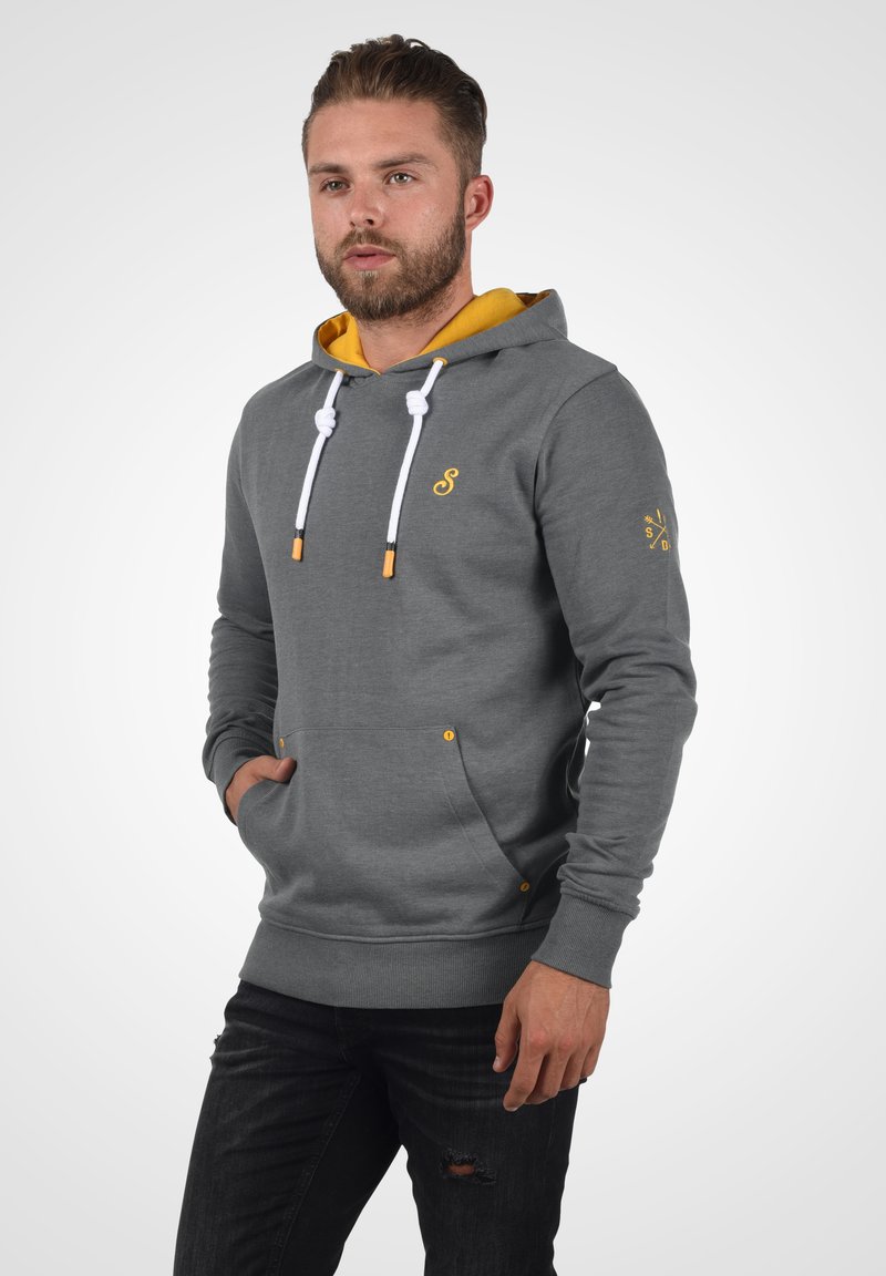 Sweat à capuche gris avec des accents jaunes, capuche et cordons de serrage. Dispose d'une poche kangourou et d'un ourlet côtelé, fabriqué en tissu doux.
