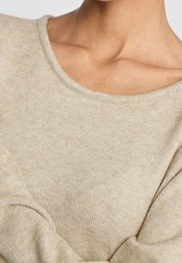 Maglione beige con scollatura ampia e tessuto a maglia texturizzato, caratterizzato da maniche leggermente a sbuffo e un aspetto morbido e accogliente.
