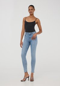 Jeans skinny azzurri chiari con vita alta, caratterizzati da piccole decorazioni in perle bianche. Abbinati a un body senza maniche nero e tacchi alti.