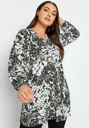 Túnica floral en blanco y negro con mangas largas tipo globo, escote en V y bolsillos laterales, hecha de un tejido ligero con una textura suave.