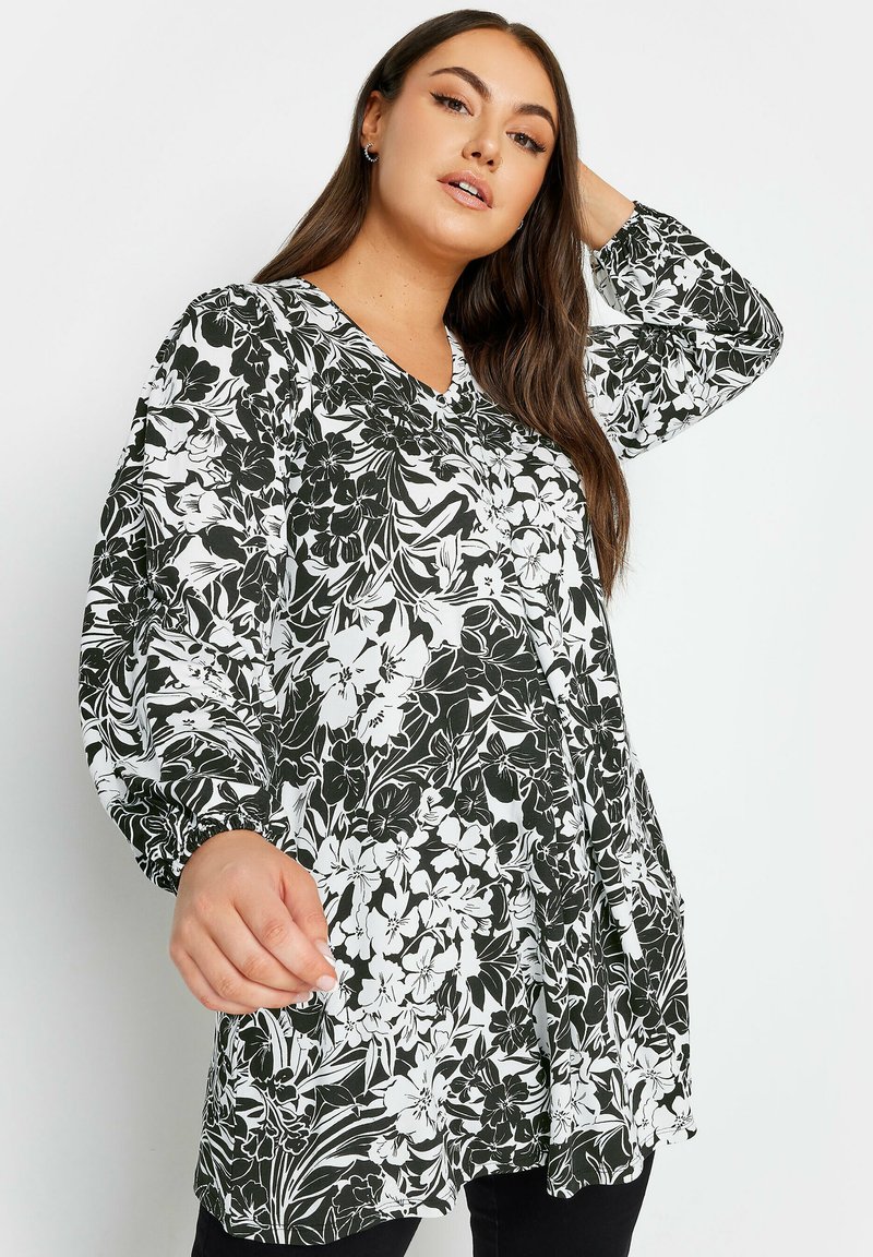 Svart och vit blommig tunika med långa ballongsärmar, V-ringning och sidfickor, tillverkad av ett lätt tyg med en mjuk yta.