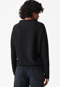 Maglione nero a trama con scollo rotondo, maniche lunghe e vestibilità comoda, abbinato a jeans scuri. Design minimalista e finitura opaca.