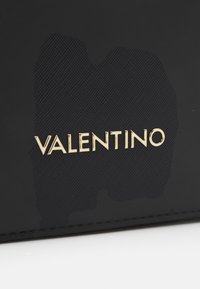 Portefeuille en matériau texturé noir, arborant un prominent logo doré "VALENTINO". Agrémenté de motifs tonaux subtils. Forme rectangulaire.