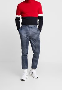 Röd och marinrandig polotröja, blå rutiga byxor med vitt rutmönster, tillsammans med vita sneakers. Avslappnad outfit med en modern design.
