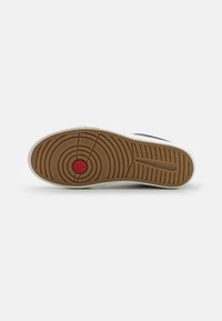 Sula av gummirubber med en unik däckmönster och en röd cirkulär detalj i mitten. Vita kanter runt sulan.