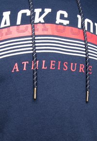 Sudadera deportiva azul marino con texto en blanco y rojo en negrita, diseño a rayas y cordones negros con puntas metálicas doradas.