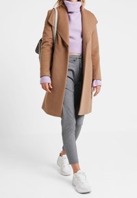 Brun ullkappa, ljuslila ribbad polotröja, grå smalbenade byxor och vita sneakers; elegant design med rena linjer och minimala detaljer.