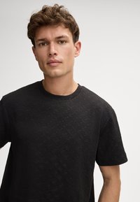 Schwarzes T-Shirt aus strukturiertem Stoff mit einem Diamantenmotiv, Rundhalsausschnitt und kurzen Ärmeln. Einfaches Design mit minimalen Akzenten.