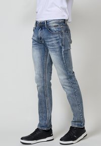 Jeans ajustados de color azul en denim deslavado con costuras en contraste. Presenta cinco bolsillos y un leve desgaste. Combinados con zapatillas deportivas negras.