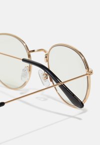 Gold metal round sunglasses with light green lenses, featuring a black temple arm and clear nose pads. Structure is sleek and minimal.