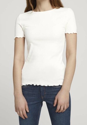 Camiseta blanca de manga corta con bordes escallopados, diseño ajustado, combinada con jeans de un azul oscuro. Textura de tela suave, diseño sencillo.