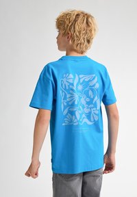 Camiseta de algodón azul con mangas cortas, que presenta un gráfico floral blanco en la parte posterior y un logo en la parte inferior. Ajuste casual.