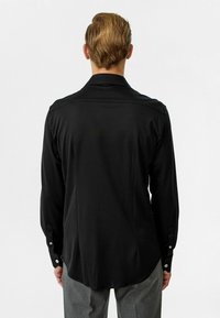 Zwarte blouse met lange mouwen van gladde stof, voorzien van een klassieke kraag, knoopmanchetten en een afgeronde zoom. Achteraanzicht met minimale details.