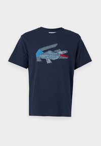 Námořnická modrá tričko s krátkým rukávem s abstraktním designem ptáka v modré, bílé a červené na hrudi.