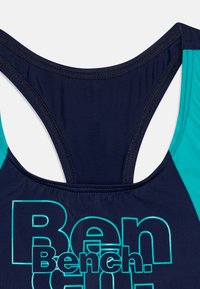 Marineblå svømmetop med racerback-design, teal accenter og fed hvid skrift, der staver "Bench." Glat tekstur og strækbart stof.