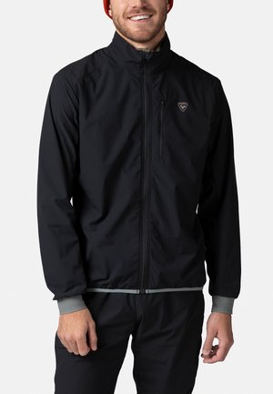 Schwarze leichte Jacke mit hohem Kragen, grauen Bündchen und einem Reißverschluss vorne. Verfügt über ein Logo-Emblem auf der oberen linken Brustseite. Glatte Textur.